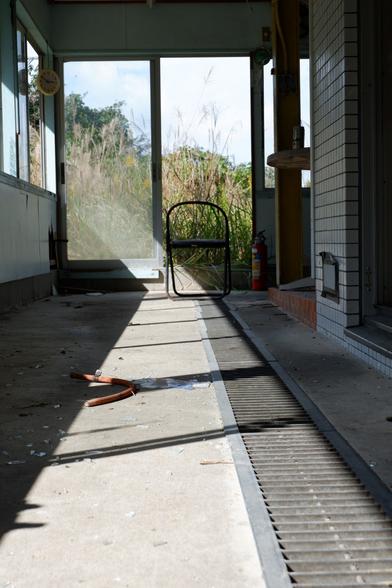 A hallway in an abandoned building. There's a chair at the other end, and sunlight from the windows on the left making a line on the floor.
