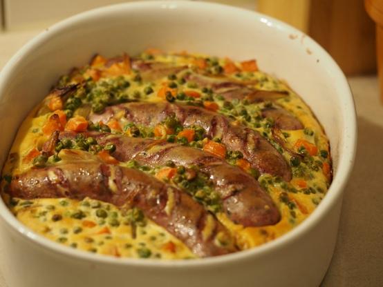 Toad in the hole - Ein britischer Auflauf mit Bratwürsten, Erbsen und Karotten in eine Art Pfannkuchenteig