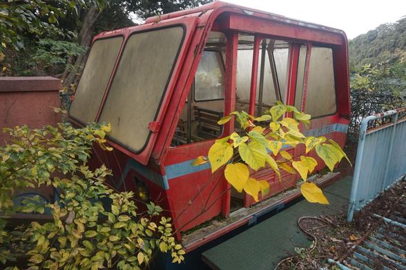 A red monorail car abandoned abs overgrown with foliage.
