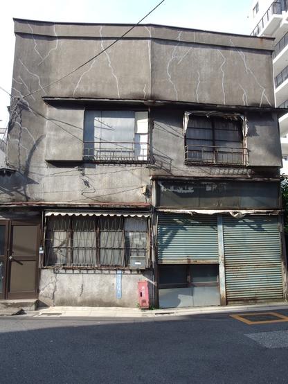 A grey building, abandoned, sits with gaping windows. The left and right are oddly different colors.