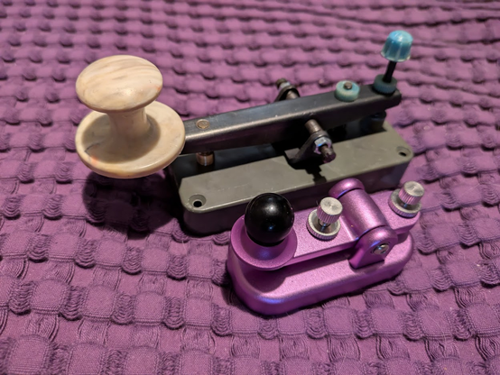 A picture of two morse code keys, one a full size Soviet era Ukrainian design, and the other a tiny purple Putikeeg brand key