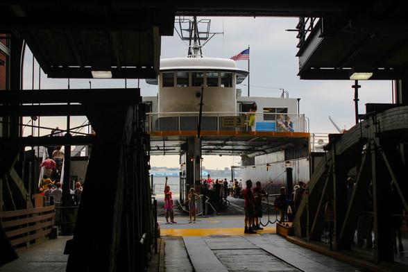 People dressed sheik and flappers all around gathered to board the ferry leading to the Governor’s Island in NY, NY for a Jazz Lawn Festival. A person at the dock waves to another on the ferry.