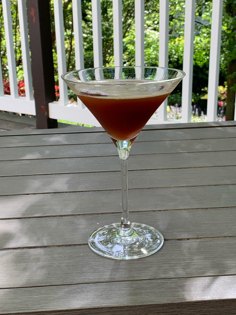 cocktail in a martini glass resting on a patio table with trees and garden in the background 