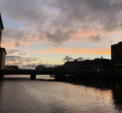 Slightly later, another angle, just a bit little darker & now the buildings are dark blocky shapes with blue sky & under lit clouds of grey and white above 