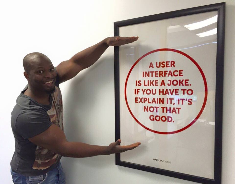 A person posing and presenting a framed poster that says, “A USER
INTERFACE
IS LIKE A JOKE.
IF YOU HAVE TO EXPLAIN IT, IT'S NOT THAT GOOD.”