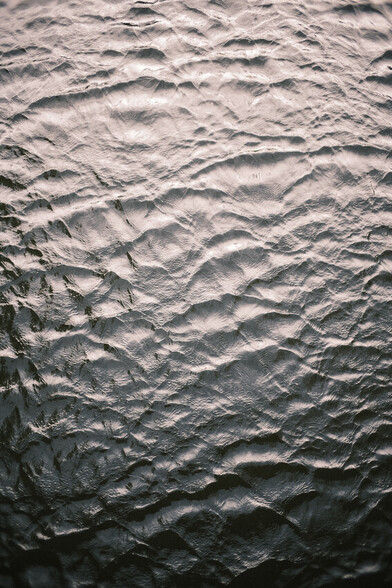 Small waves photographed from above. They look like rock formations or some other glassy texture. Gradient brightness from top to bottom, bottom being the darkest.