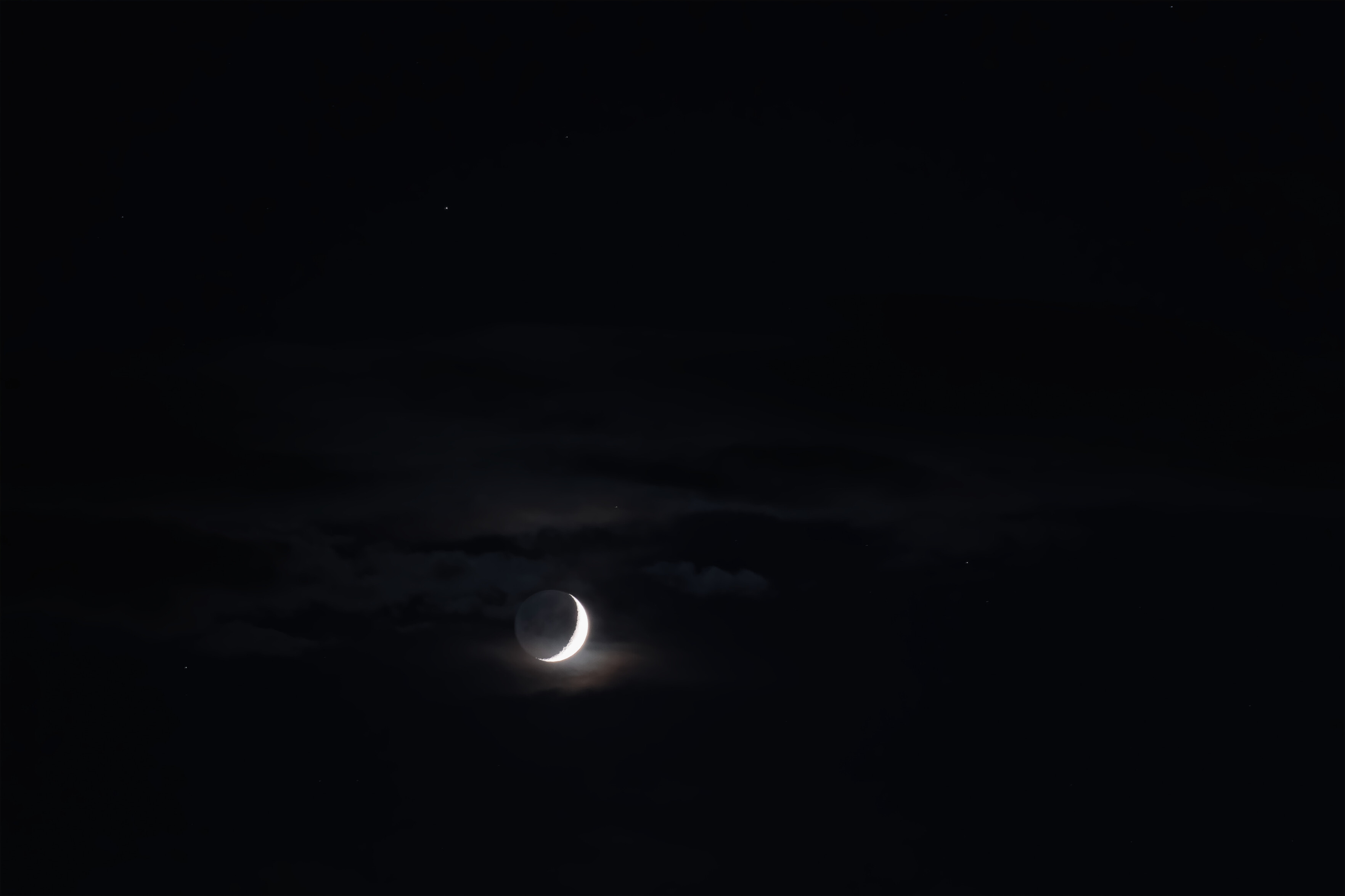 Crescent moon poking out behind clouds