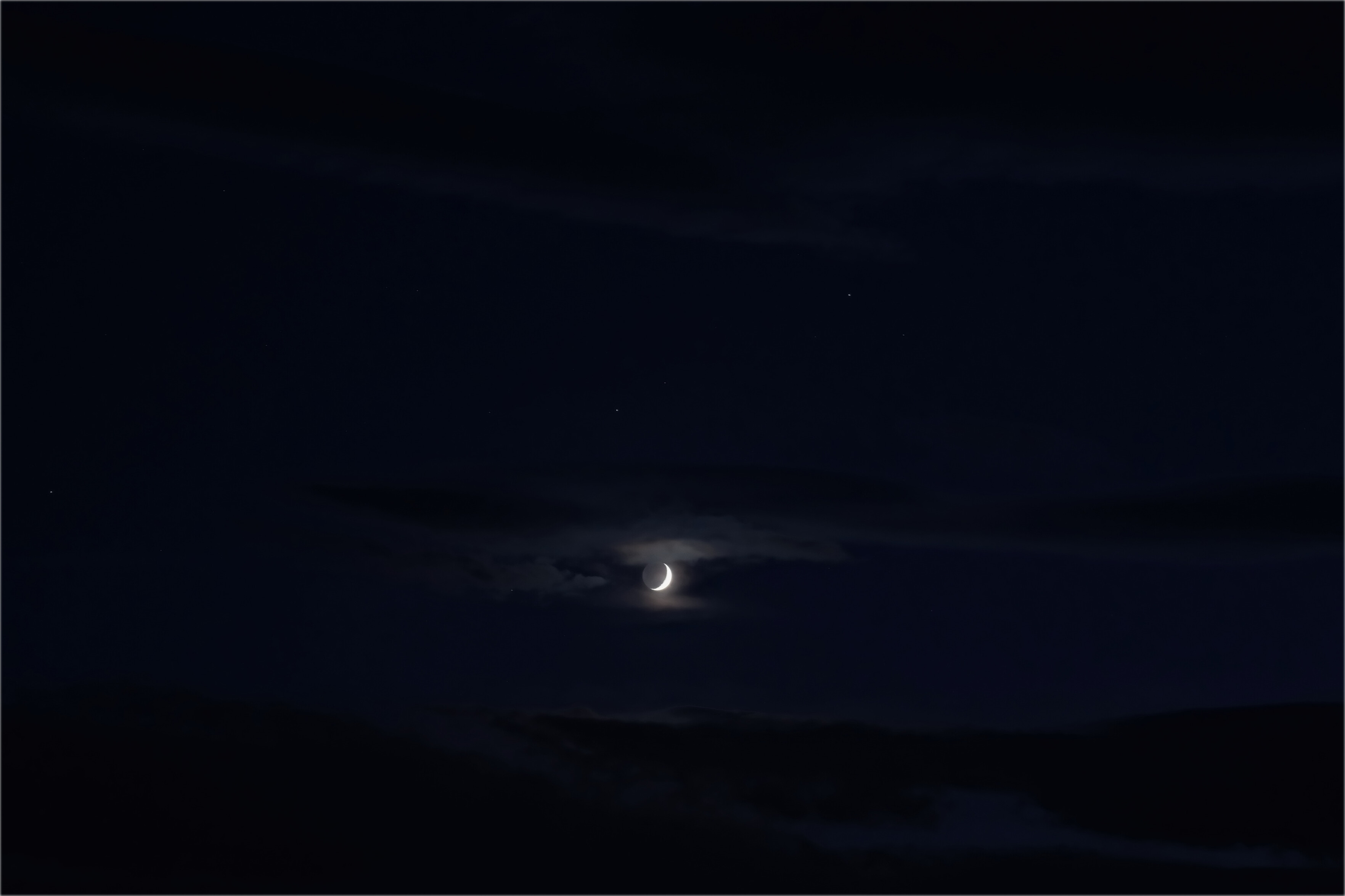 Crescent moon poking out behind clouds