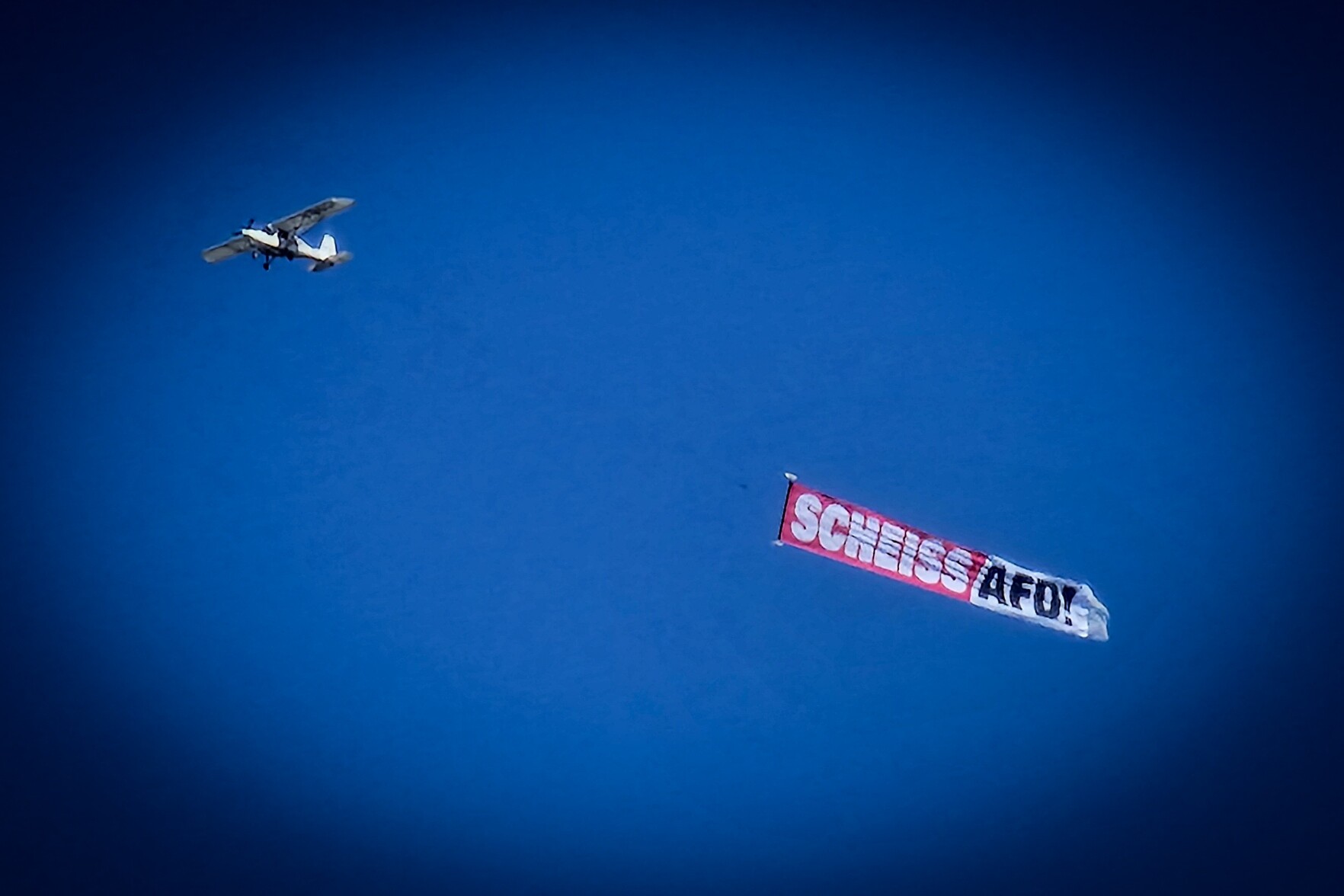 Ein Flugzeug am Himmel, das ein Spruchband mit der Aufschrift "Scheiss AfD" zieht.