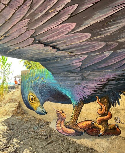 Streetartwall. A mural of a bird of prey pouncing on a snake is sprayed/painted on a side wall and the ceiling under a bridge. The green and yellow head of the bird and the brown snake are sprayed on the side wall. The ceiling is filled with the bird's purple wings. A simple but impressively well done mural with 3D effect over 2 walls.