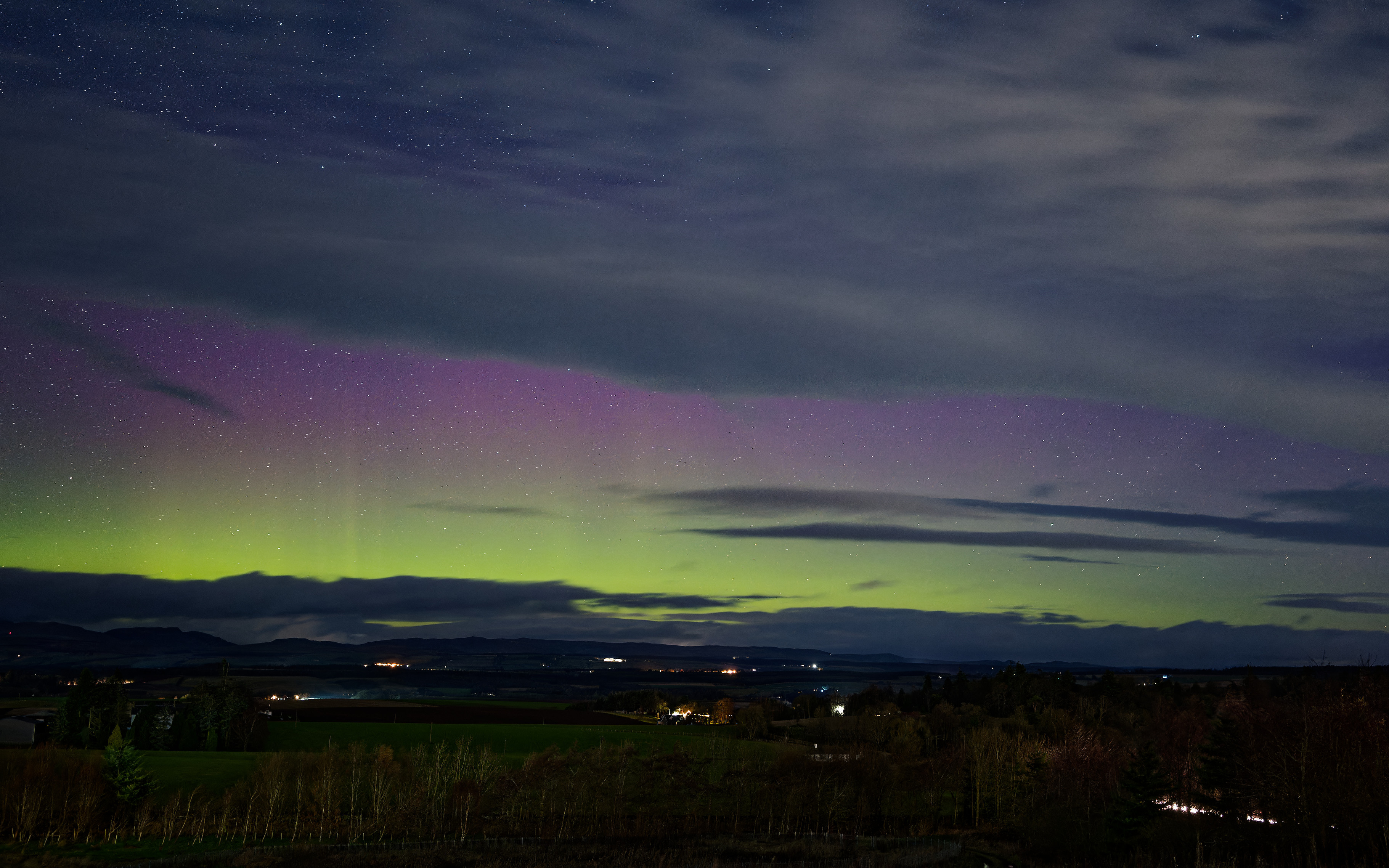 Aurora borealis display over Perthshire showing much cloud, some purple and green with rays.