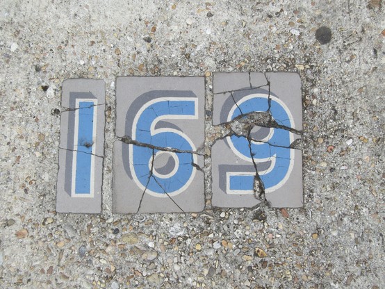 concrete sidewalk with cracked old tiles of numbers, light blue on light grey, reading "169"