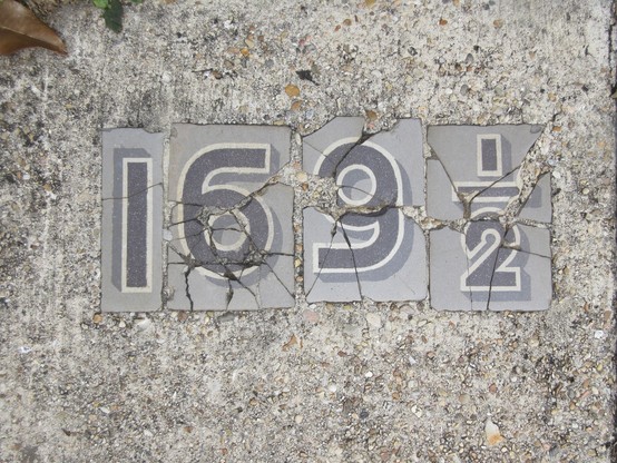 concrete sidewalk with cracked old tiles of numbers, dark grey on light grey, reading "169 1/2"