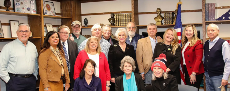 A photo of 16 people standing together in a room, the walls adorned with sparsely-filled bookcases. Most of the people are lily-white, most of them are older, and almost all of them are smiling. These are the fake Republican electors from Michigan, who signed and submitted forged and fraudulent documents claiming they were Michigan's electors for Donald Trump. Trump had, in fact, lost the state of Michigan, and the real electors for Joe Biden had already been certified.