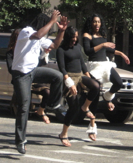 Scene in urban street. Three women and one man are happily dancing, leaping high into the air. 