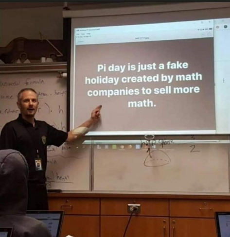 A man is standing at the head of a classroom in front of a projector screen. On the screen is a document that says "Pi day is just a fake holiday created by math companies to sell more math."