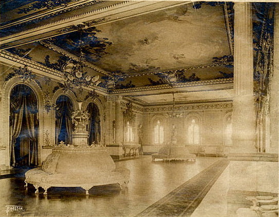 Sepia photo of elaborate building interior with high ceiling with murals, neo-classical columns, circular plush benches, arch windows and doorways, all adorned with busy detail ornaments in high budget late 19th-century style. 