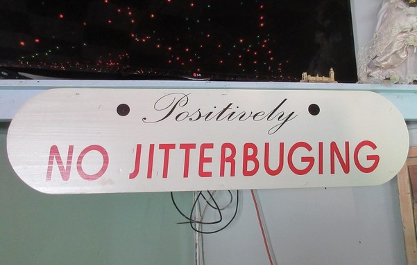 Sign with white background. Top row, black lettered cursive script: "Positively"
Bottom row in larger block red letters: "NO JITTERBUGGING"
