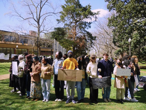 Thirteen visible students and others behind them link arms to surround a protest wall on Vanderbilt University's campus.