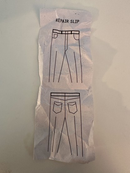 A crumpled repair slip with simple line drawings of pants on it.