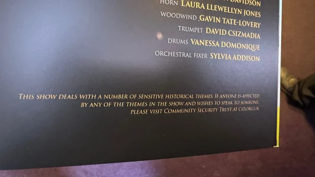 A picture of a poster for a work of musical theatre.  Underneath the tail end of a list of musician credits, there is a trigger warning reading: 