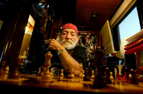 Willie Nelson, wearing his signature red bandana, looks over a chess board.