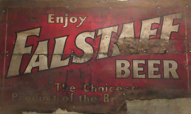 badly faded wooden sign, white letters on red background. 

Text: "Enjoy FALSTAFF BEER - The Choicest Product of the Br". (rest of sign illegible.) 