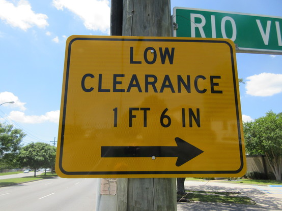 Metal sign on utility pole beside street, yellow background with black letters.  At bottom an arrow symbol points right. 

Text: "LOW CLEARANCE - 1 FT 6 IN". 