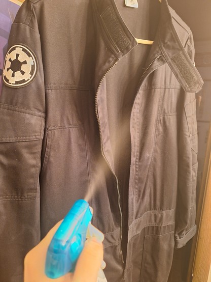 Black imperial flightsuit being sprayed with a small bottle of diluted vodka for sterilization purposes