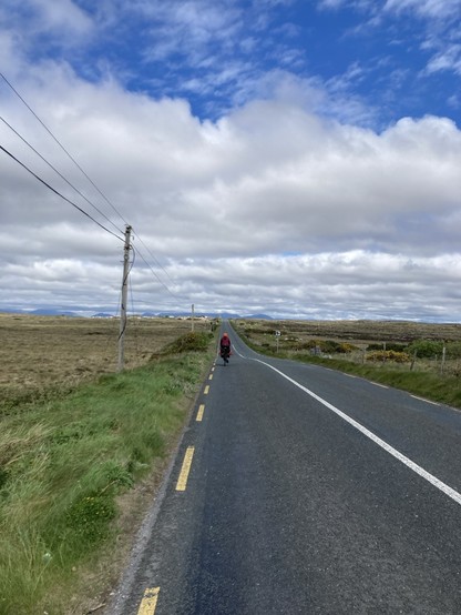 A straight road towards mountains with a cyclist in the distance 