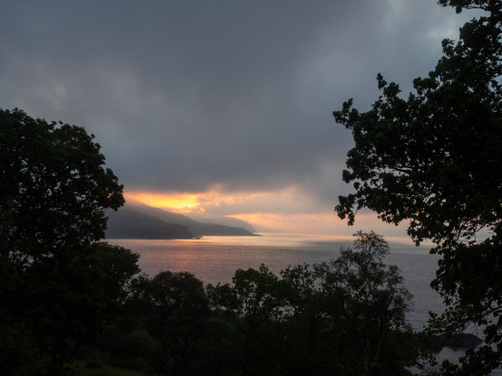 Sunrise over a coastal headland framed by trees. Over three photos the sun rises from behind the headland creating a narrow band of golden light, passes into dark cloud, and then breaks through to thinning cloud.