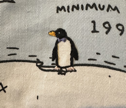 A small embroidered penguin wearing a purple bow tie 
