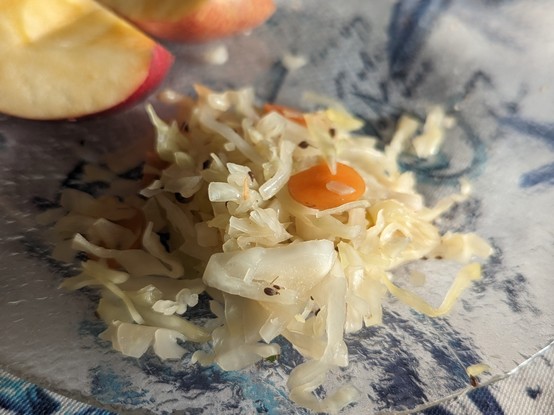 Small pile of sauerkraut - shredded cabbage and small bits of orange carrot, with flecks of spice/seed, on a plate