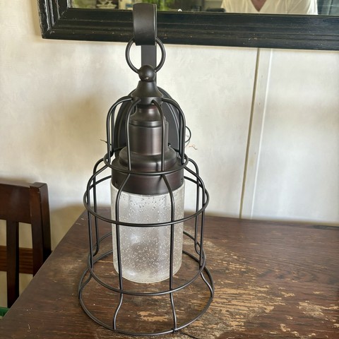 An outdoor wall sconce with an elongated, dirty, bubble glass globe and a cage around it. 