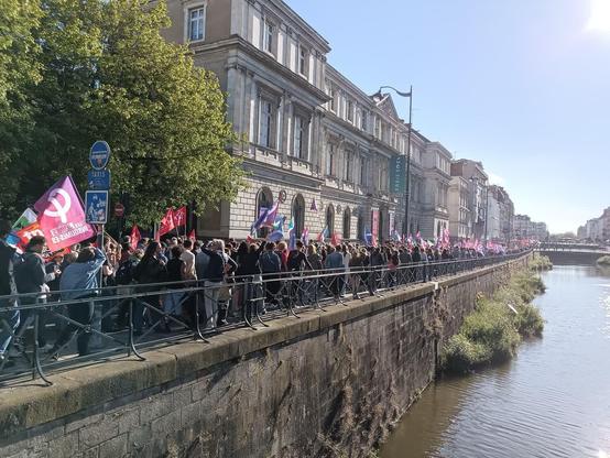 Photo de la manifestation prise depuis un pont sur la Vilaine et qui montre bien que le quai est plein.
Il y a des drapeaux de toutes les organisations syndicales ainsi que de plusieurs partis politiques de gauche.