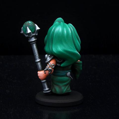 A painted miniature of a mage.  It is a chibi-style figure with large head and small body.  Her hair and dress are shades of green, and she is holding a silver staff decorated with a green crystal ball.