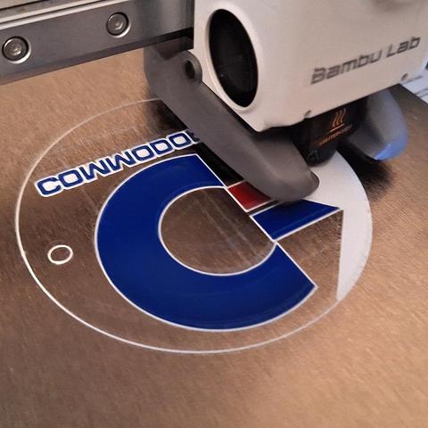 Picture of a 3D-printer (Bambulab A1 Mini + AMS lite) printing a suction cup sign with a Commodore 64 motiv.