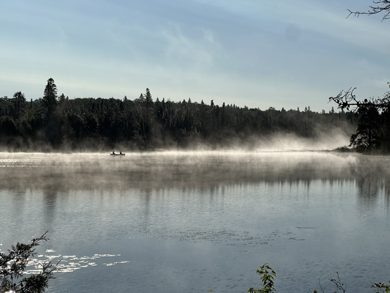 Two people fishing in a canoe in the morning fog