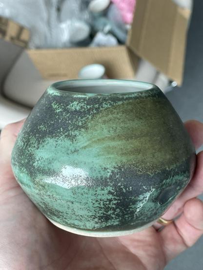 A decorative vase shaped like two small bowls one inverted atop the other, also glazed in copper green with larger, more substantial metallic patches, and a brushed patch of another glaze layered on top that shows as a green/gold on the upper face.