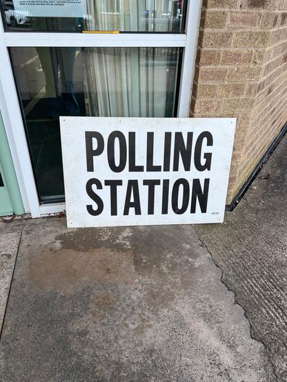 A sign labelled “polling station” propped up beside a glass door.