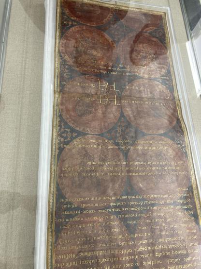 A medieval document featuring Latin text and several circular illustrations. The manuscript is displayed under glass for preservation.