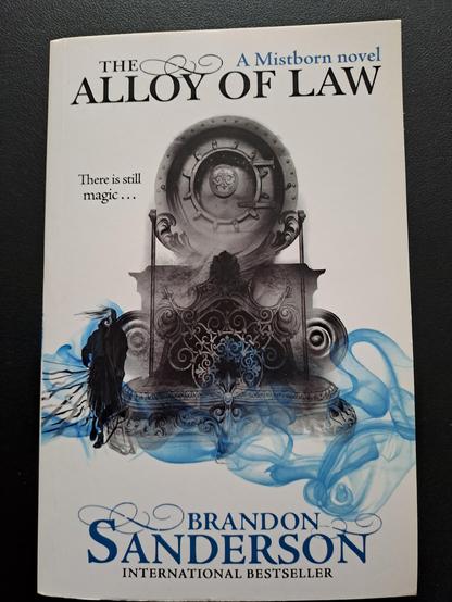 The cover of the book.

A shadowy man stands to the side of an old fashioned but fancy metal vault door atop a pedestal, while blue mist swirls along the bottom of the image.