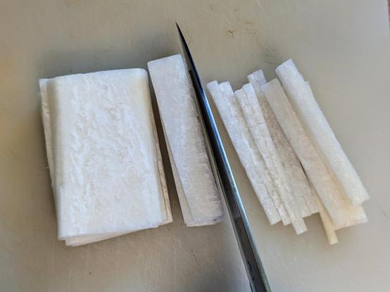 Top view of a rectangular block of white daikon that has lots of horizontal slices.
A small block has been cut through from the top with a knife in the picture, yielding thin julienne strips.