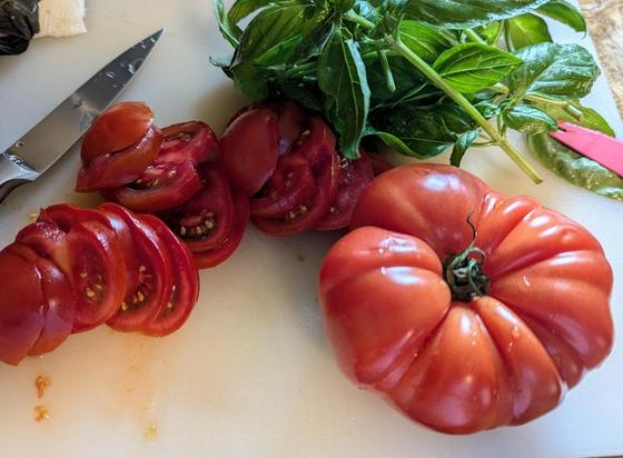 Sliced  'campari' tomatoes and a big uncut heirloom tomato all gnarly on a cutting board next to a bunch of basil