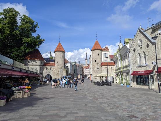 Une entrée de la vieille ville de Tallinn, Estonie. De part et d'autre d'une rue piétonne, deux tours médiévales. Le ciel est bleu avec quelques nuages.