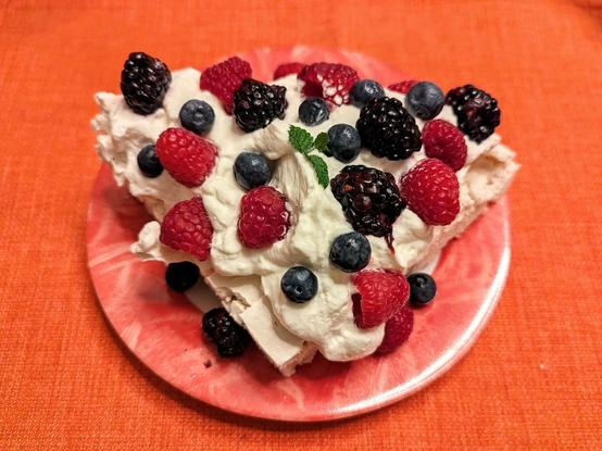 A quarter of the round Pavlova with fresh whipped cream and topped with blackberries, raspberries and blueberries