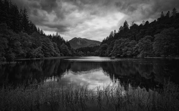Conventional view of Glencoe Lochan with clouds reflected in the water, dark moody black & white 