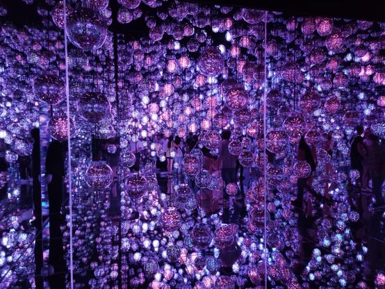 A photo from the teamLab Borderless exhibition in Tokyo, showing a dark room filled with - at this moment (they change color) - purple balls, hanging from the ceiling.