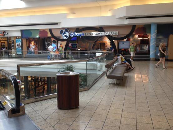 A section of a shopping mall with people walking and sitting on benches. A store named 