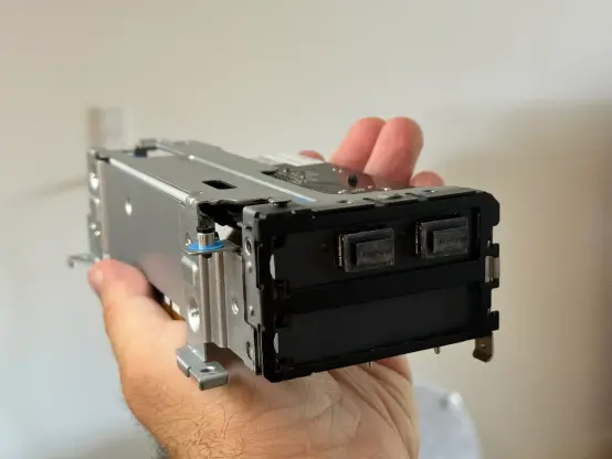 A hand holding up a PCIe network card mounted in a PCIe GPU riser cage